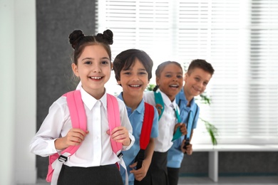 Photo of Happy children in school uniform with backpacks indoors