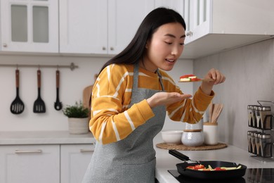 Photo of Beautiful woman cooking and tasting vegetable dish in kitchen. Space for text