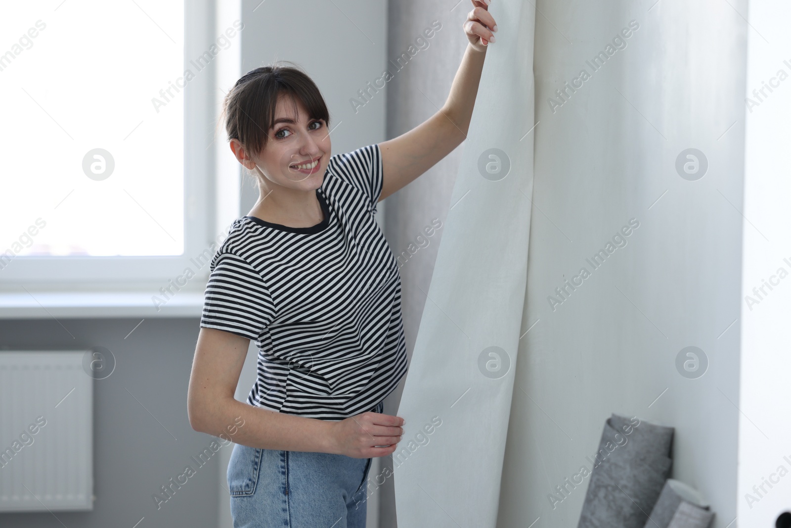 Photo of Woman hanging stylish gray wallpaper in room