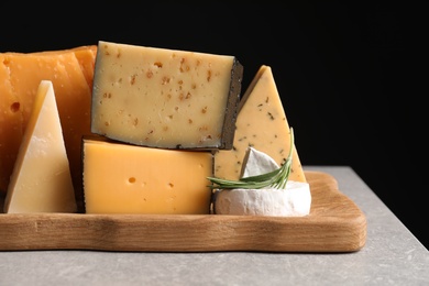 Photo of Wooden tray with different sorts of cheese and rosemary on grey table against black background, space for text