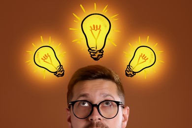 Image of Idea generation. Man looking at illustrations of glowing light bulb over him on dark golden background