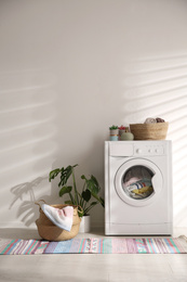 Photo of Modern washing machine and wicker basket with laundry near white wall. Interior design