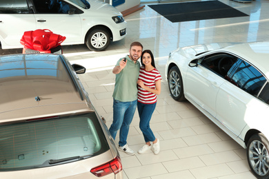 Photo of Happy couple with car key in modern auto dealership