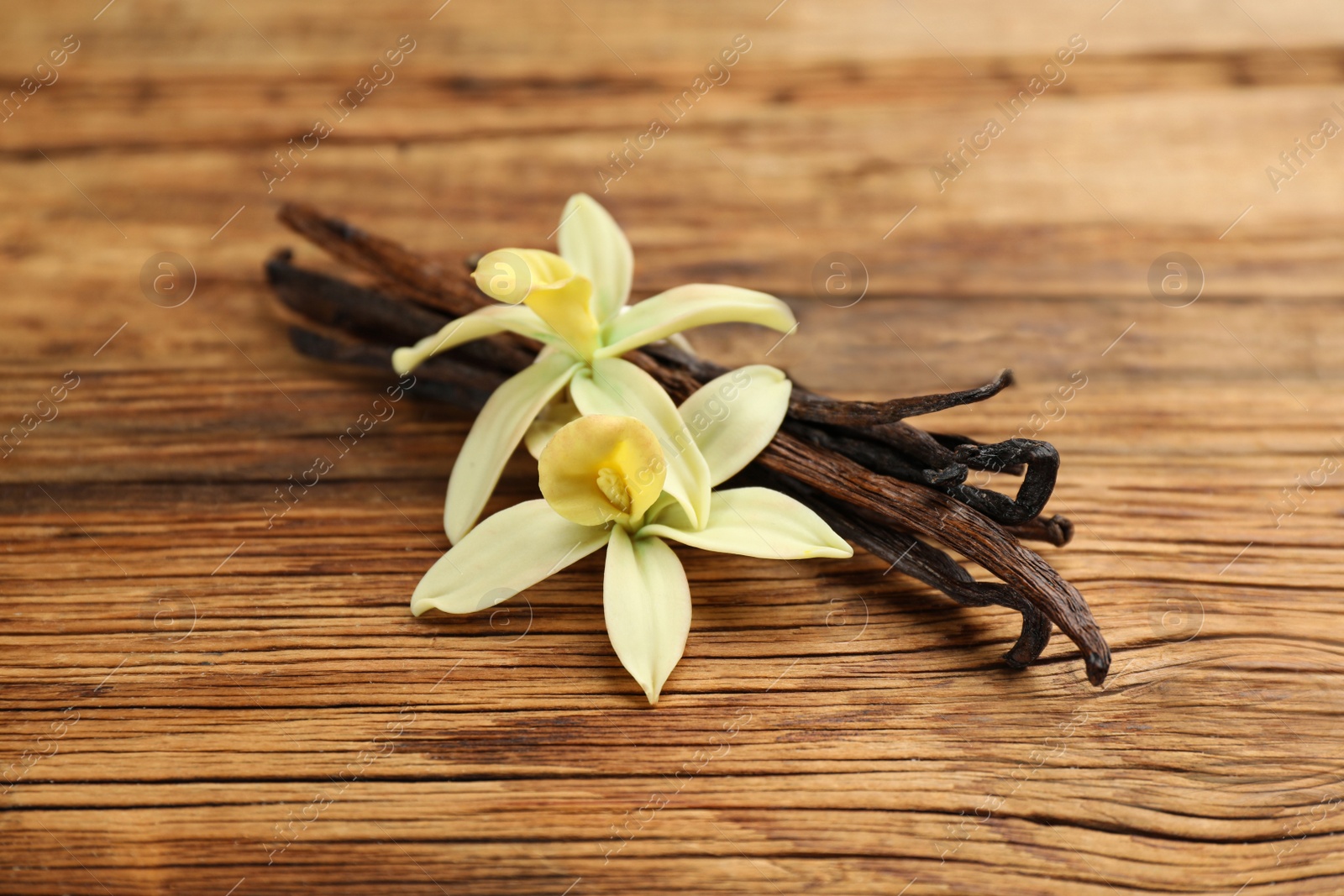 Photo of Aromatic vanilla sticks and flowers on wooden table, closeup