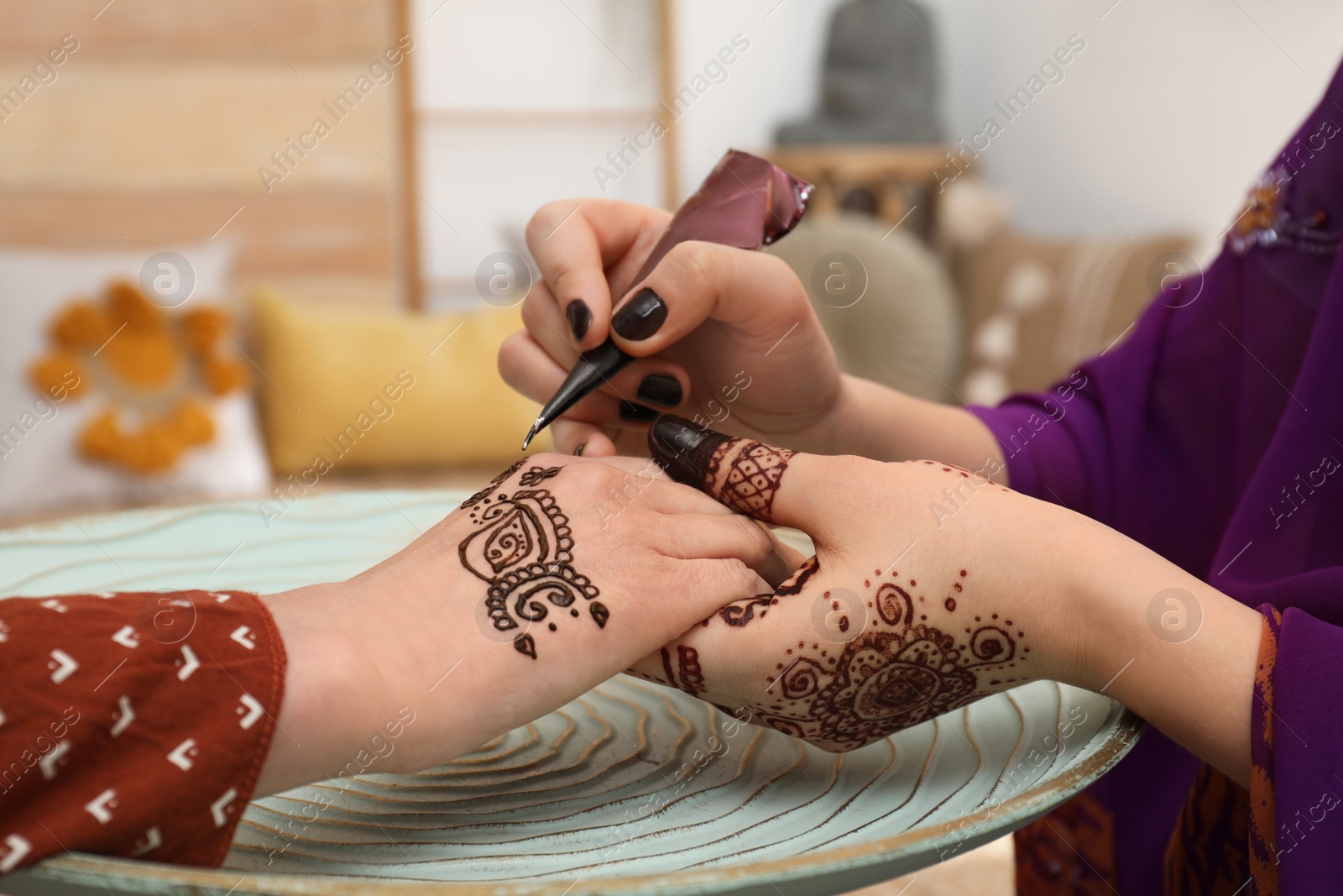 Photo of Professional mehndi master making henna tattoo indoors, closeup