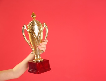 Photo of Child holding golden winning cup on red background, closeup. Space for text