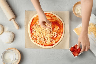 Photo of Woman adding cheese to pizza on table, top view