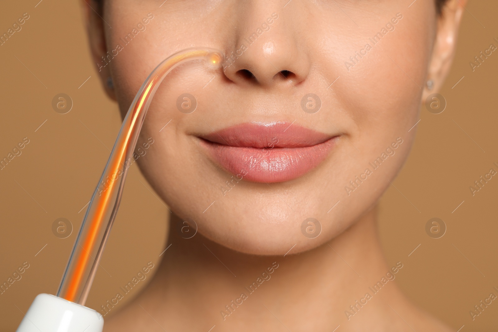 Photo of Woman using high frequency darsonval device on beige background, closeup