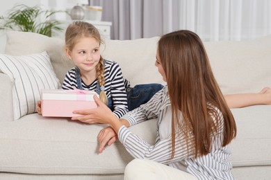 Photo of Cute little girl presenting her mother with gift on sofa at home