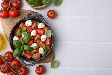 Tasty salad Caprese with mozarella balls, tomatoes and basil on white tiled table, flat lay. Space for text