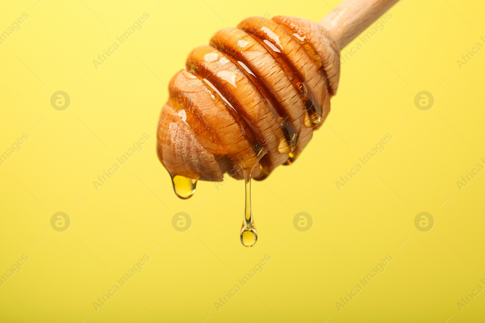 Photo of Delicious honey flowing down from dipper against yellow background, closeup. Space for text