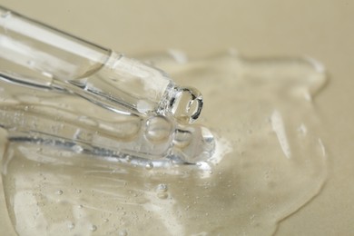 Pipette with cosmetic serum on beige background, closeup