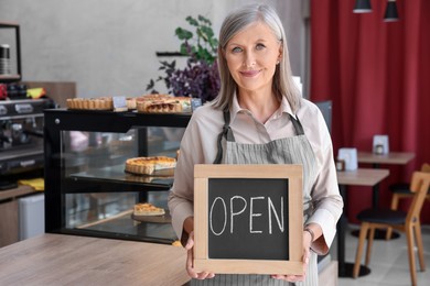 Photo of Smiling business owner holding open sign in her cafe, space for text