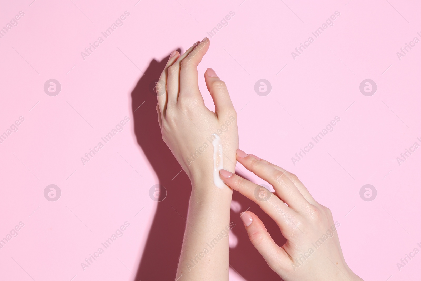 Photo of Woman applying cream on her hand against pink background, closeup