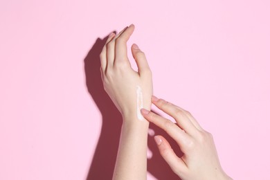 Woman applying cream on her hand against pink background, closeup