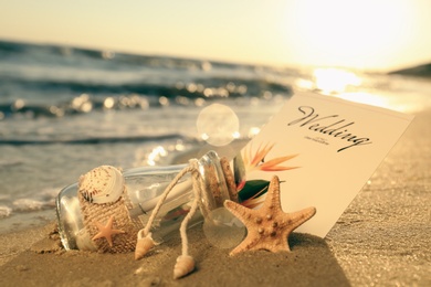 Photo of Wedding invitation and glass bottle on sandy beach at sunset