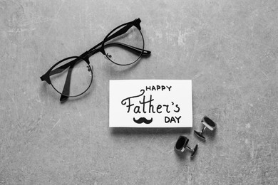 Photo of Card with phrase Happy Father's Day, glasses and cuff links on light grey background, flat lay