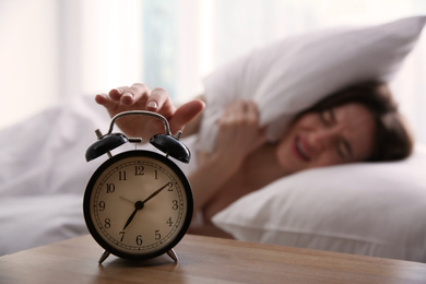 Young woman turning off alarm clock at home in morning, focus on hand