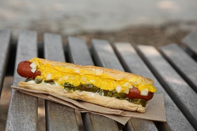 Photo of Fresh tasty hot dog with sauce on wooden surface outdoors