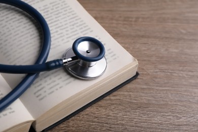 Photo of Student textbook and stethoscope on wooden table, closeup. Medical education