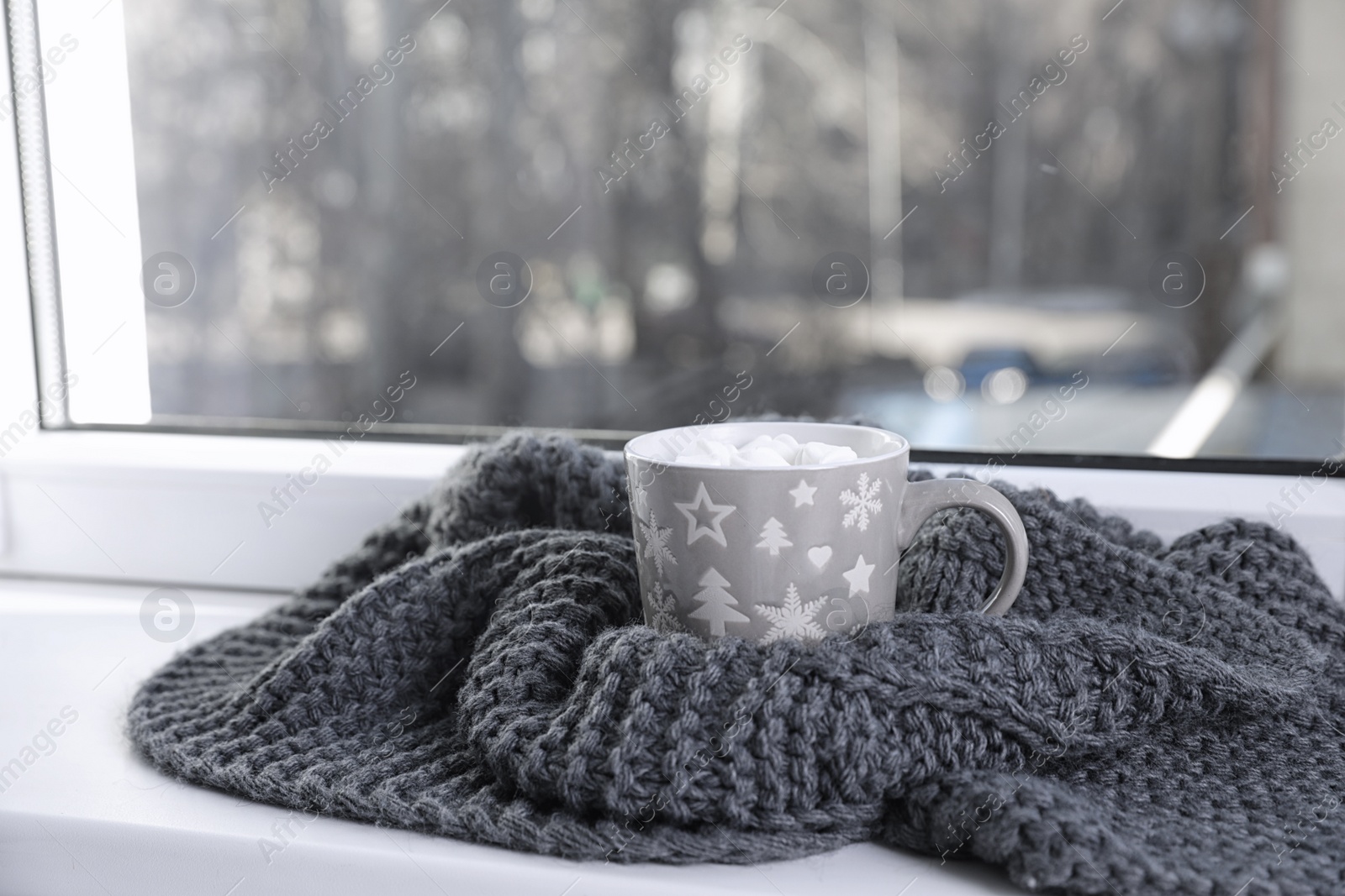 Photo of Cup of winter drink and knitted scarf on windowsill. Space for text