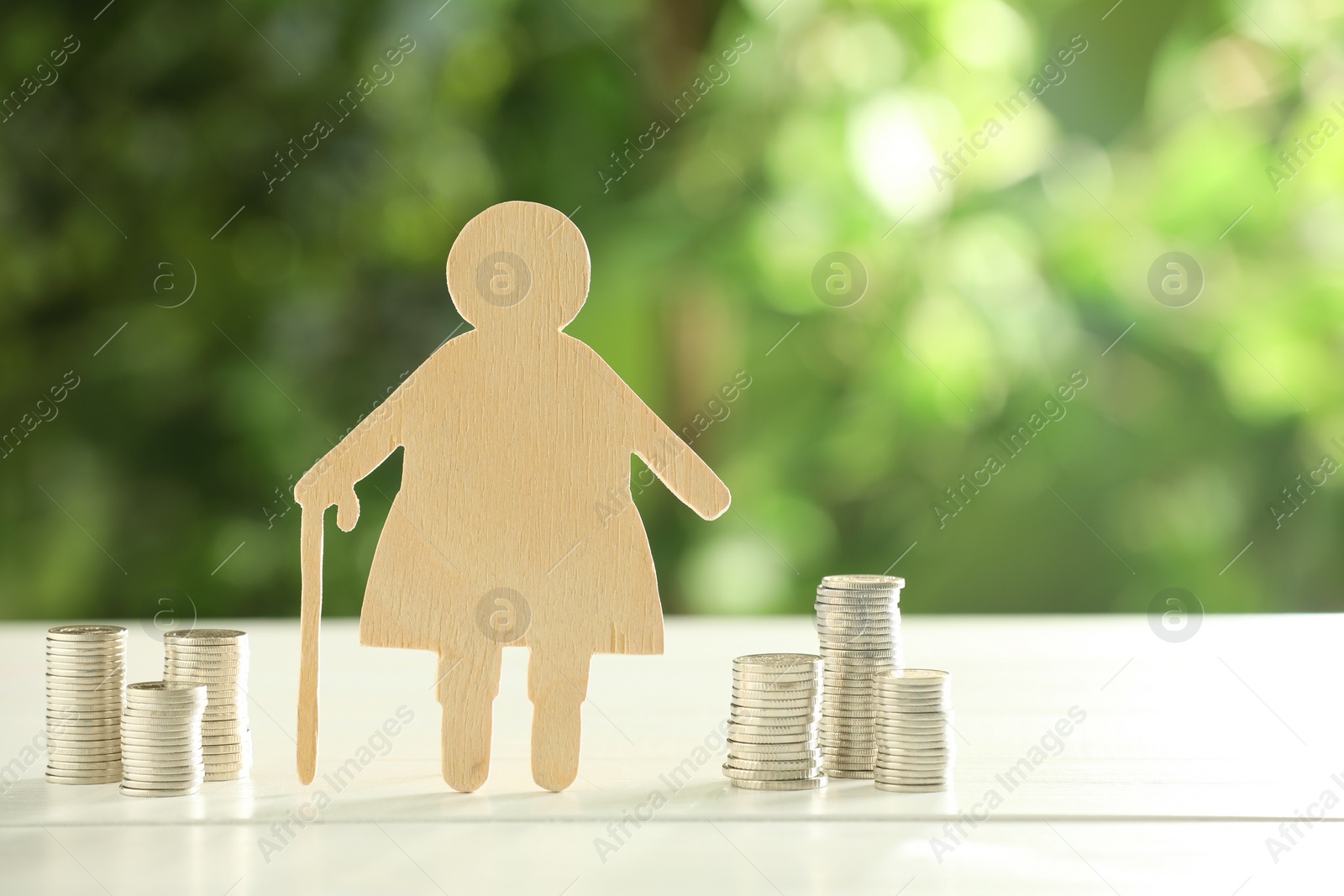 Photo of Pension savings. Figure of senior woman and stacked coins on white wooden table outdoors