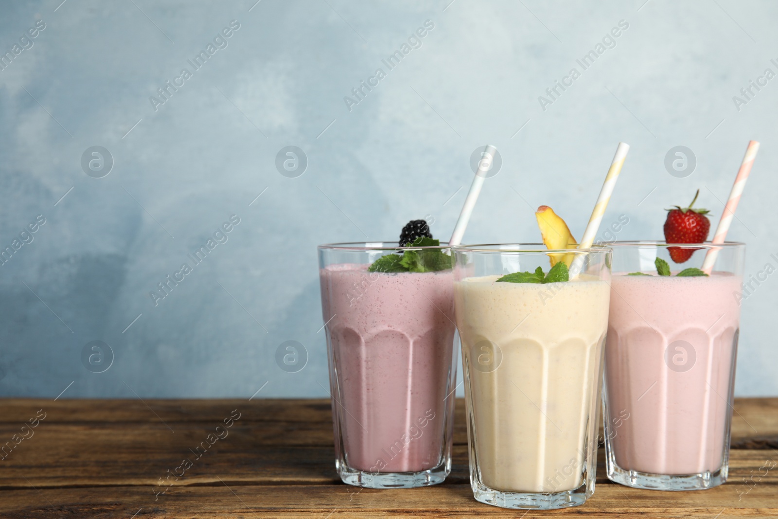 Photo of Different tasty milk shakes on wooden table. Space for text