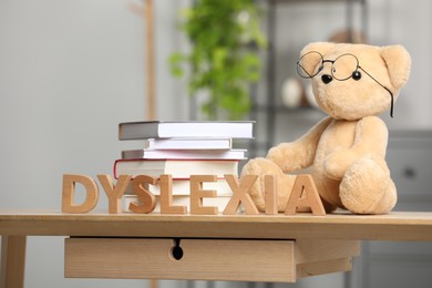 Photo of Teddy bear in glasses, books and word Dyslexia made of letters on wooden table indoors