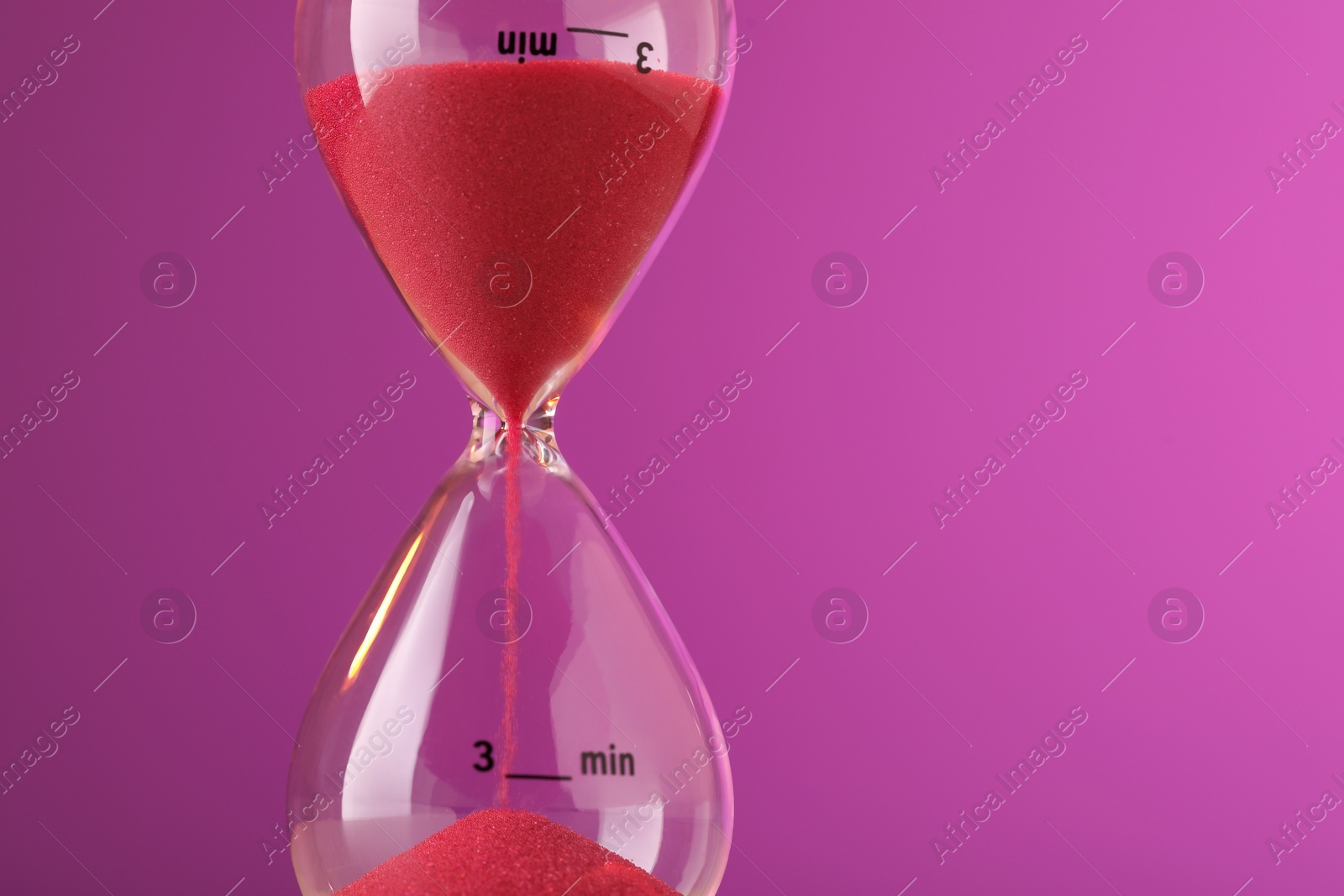 Photo of Hourglass with flowing red sand on violet background, closeup. Space for text