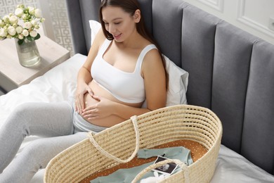 Photo of Beautiful pregnant woman making heart with hands on bed indoors