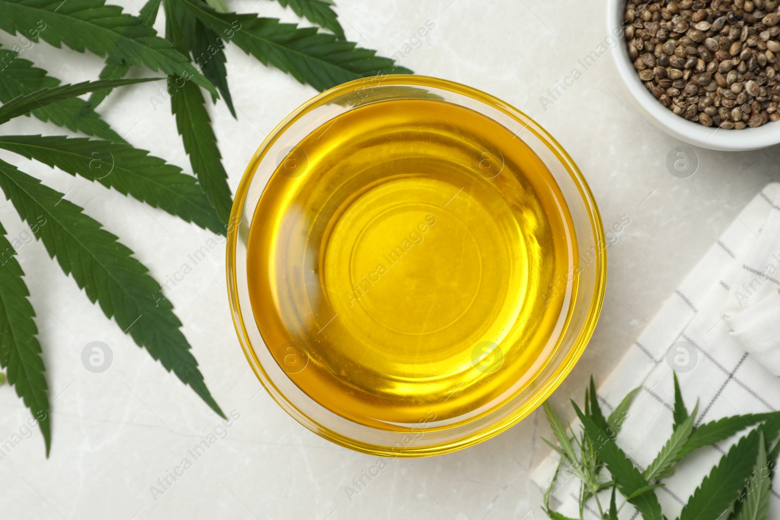 Photo of Hemp oil, seeds and leaves on light grey marble table, flat lay