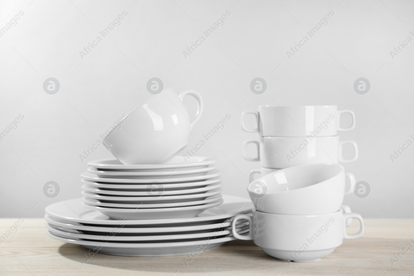 Photo of Set of clean dishware on white wooden table against light background