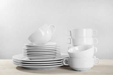 Photo of Set of clean dishware on white wooden table against light background