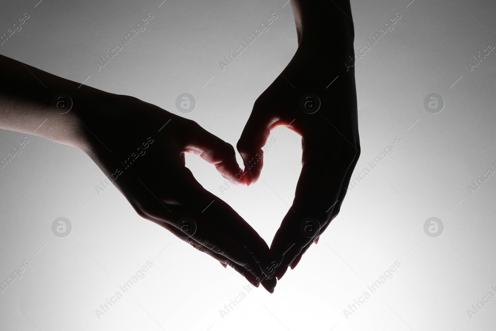 Photo of Woman making heart gesture on light background, closeup