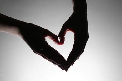 Woman making heart gesture on light background, closeup