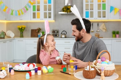 Photo of Father and his cute daughter painting Easter eggs at table in kitchen