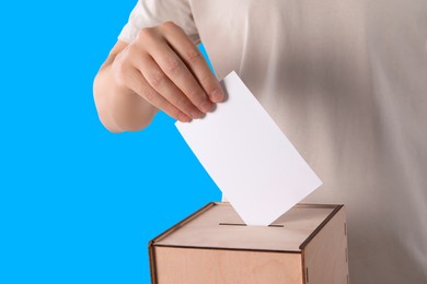 Man putting his vote into ballot box on light blue background, closeup