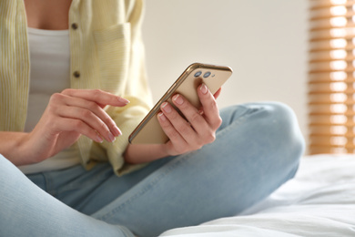 Young woman using modern smartphone on bed at home, closeup