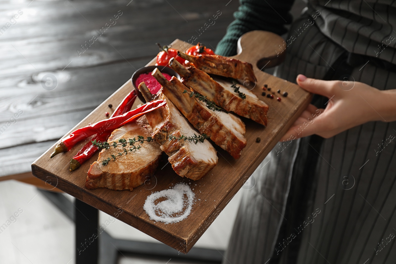 Photo of Woman holding serving board with delicious roasted ribs, closeup