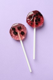 Sweet colorful lollipops with berries on lilac background, flat lay