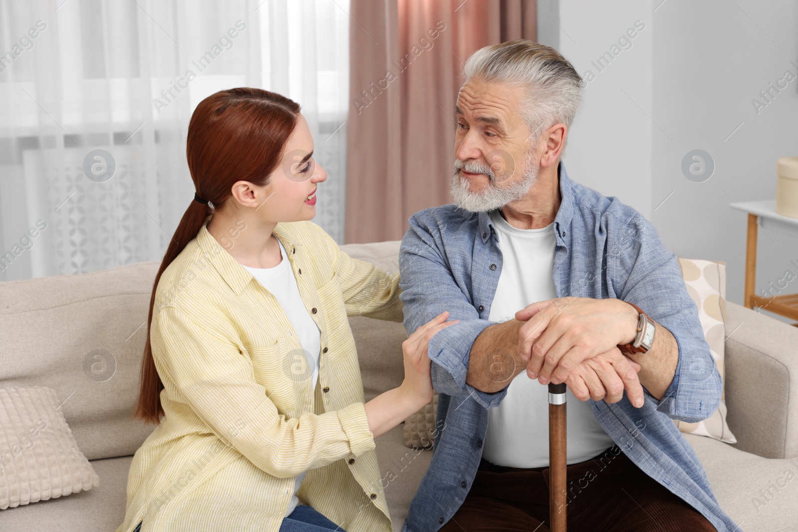 Photo of Caregiver and senior man with walking cane on sofa at home