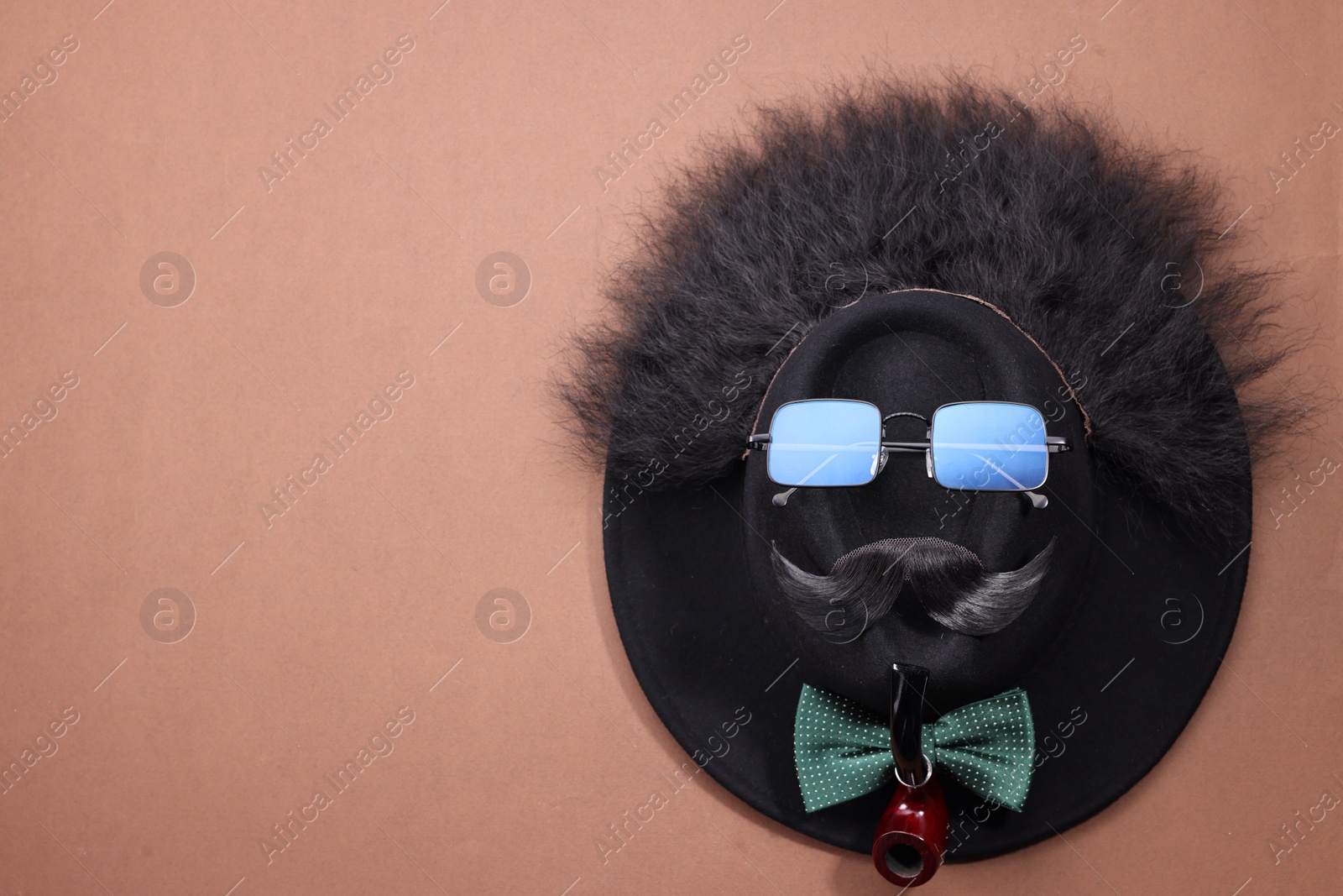 Photo of Man's face made of artificial mustache, sunglasses and hat on brown background, top view. Space for text