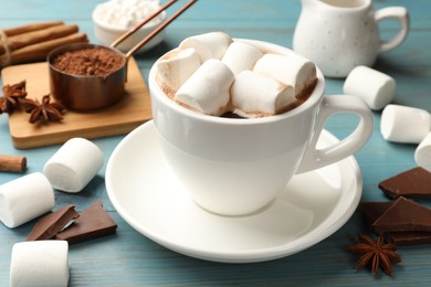 Tasty hot chocolate with marshmallows and ingredients on light blue wooden table, closeup