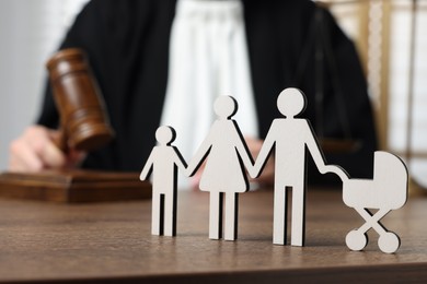 Photo of Family law. Judge with gavel sitting at wooden table, focus on figure of parents and children