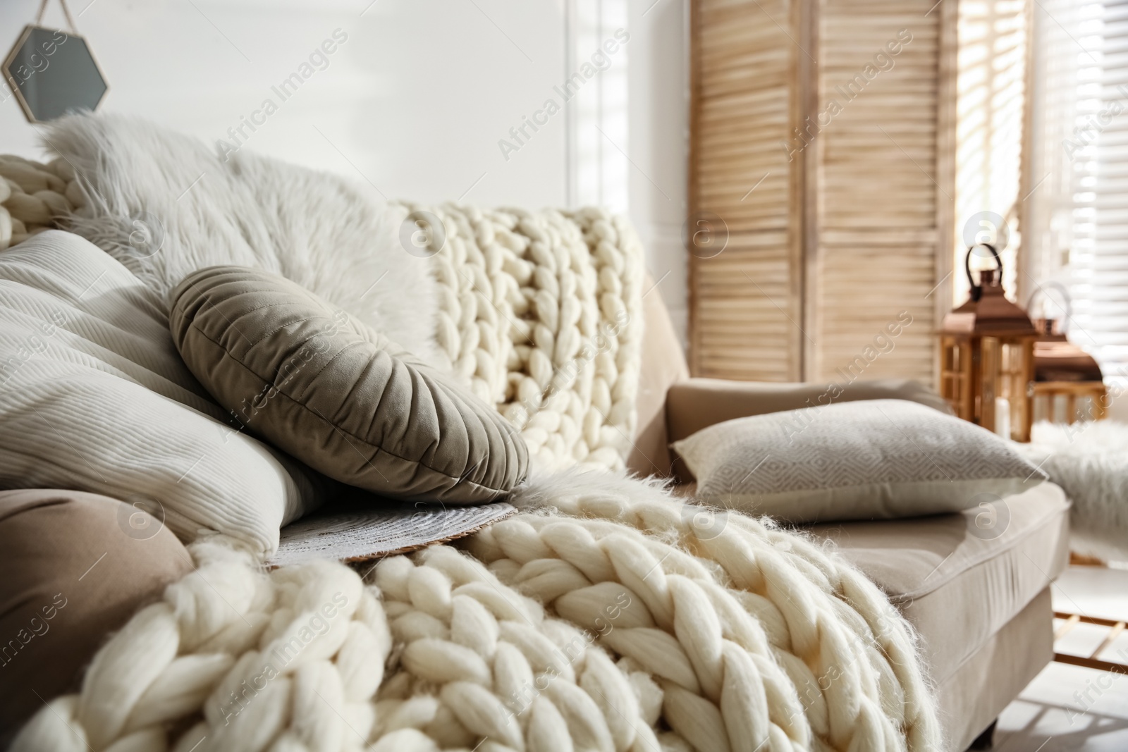 Photo of Beige sofa with knitted blanket and cushions in room. Interior design
