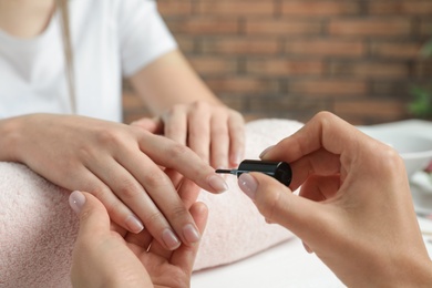 Photo of Manicurist applying polish on client's nails at table, closeup. Spa treatment