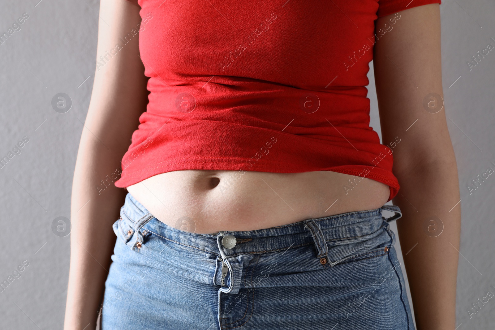 Photo of Woman wearing tight clothes on grey background, closeup. Overweight problem