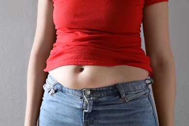 Woman wearing tight clothes on grey background, closeup. Overweight problem