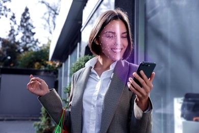 Woman using smartphone with facial recognition system on street. Security application scanning her face for approving owner's identity