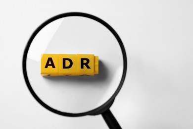 Image of Alternative dispute resolution. Top view through magnifying glass on yellow cubes with letters ADR, white background